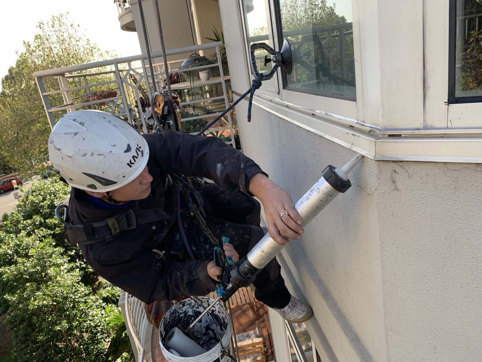 Mission Possible technician applying sealant to a window frame while suspended on rope