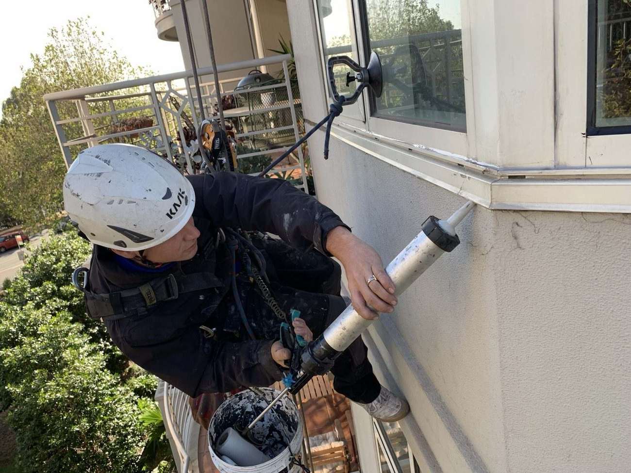 Mission Possible technician applying sealant to a window frame while suspended on rope
